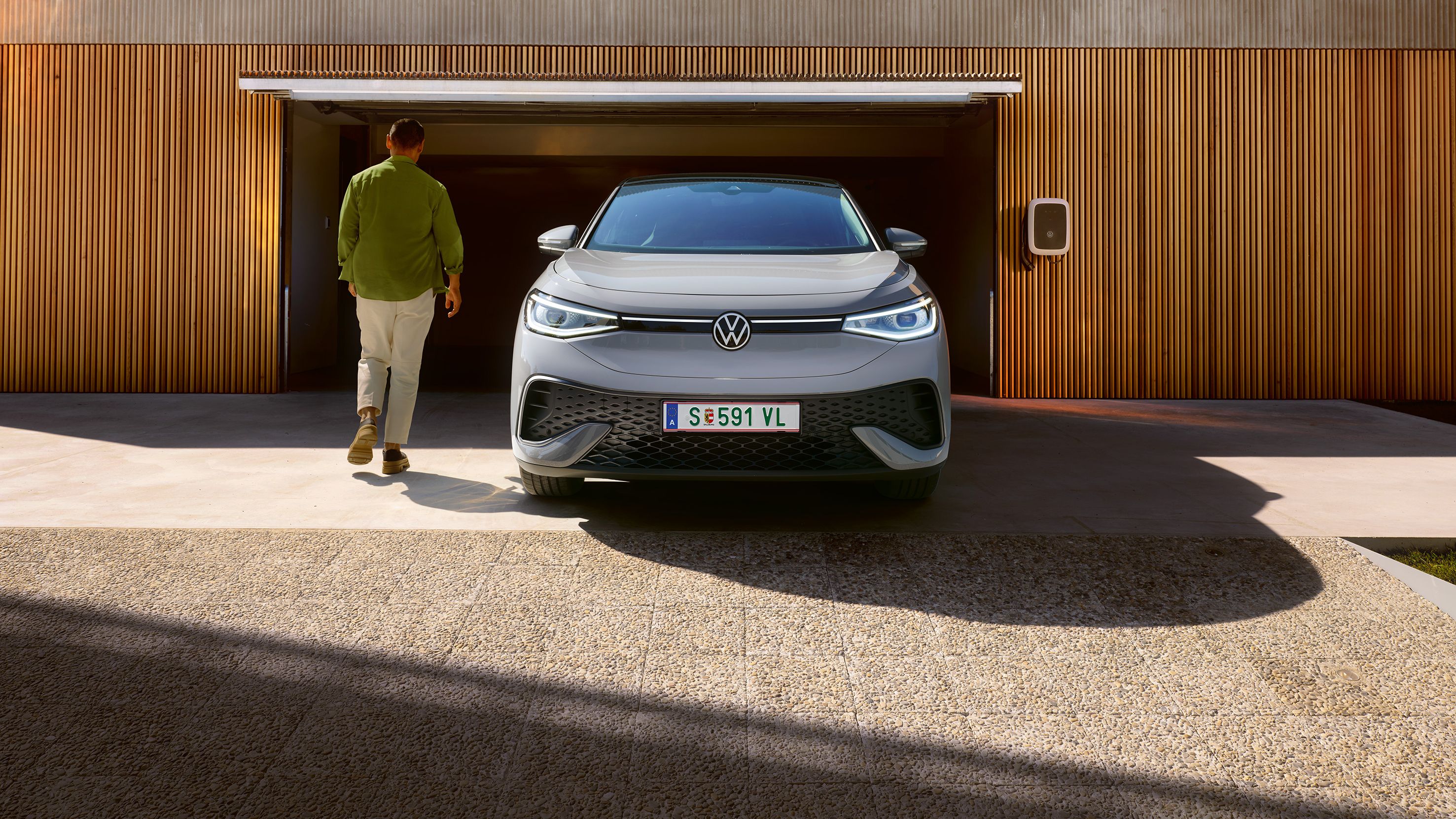 Frontansicht eines grauen VW ID.5 der vor Garage steht, Mann geht an ihm vorbei