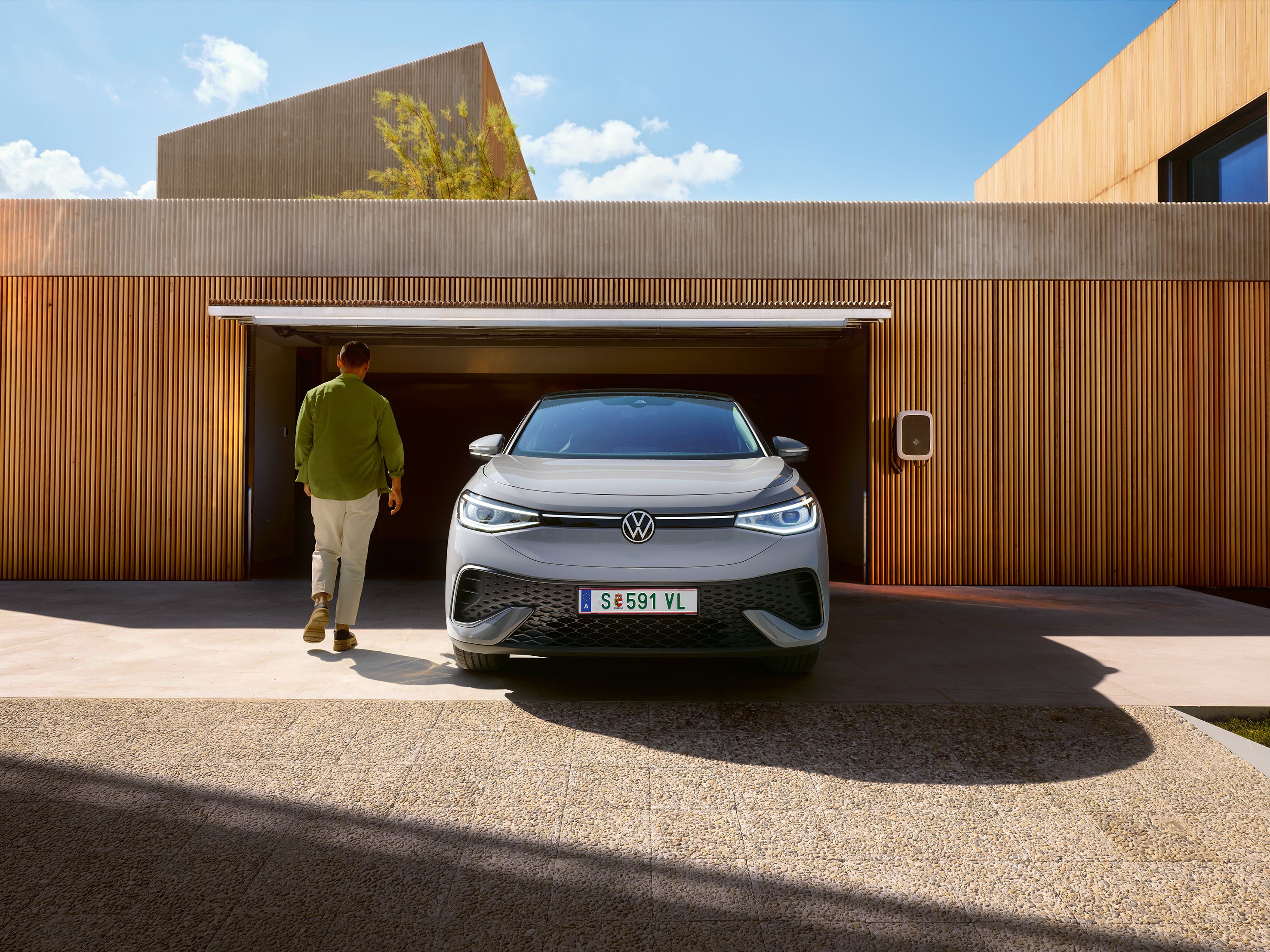 Frontansicht eines grauen VW ID.5 der vor Garage steht, Mann geht an ihm vorbei