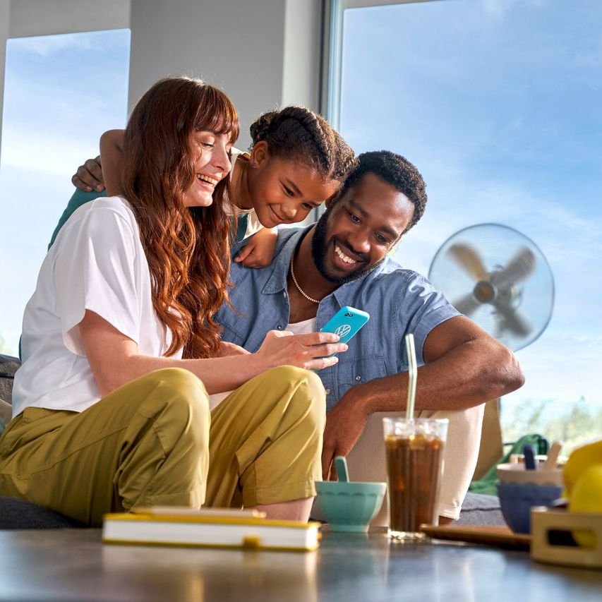 Eine Familie sitzt auf dem Sofa und schaut glücklich in ein Smartphone.
