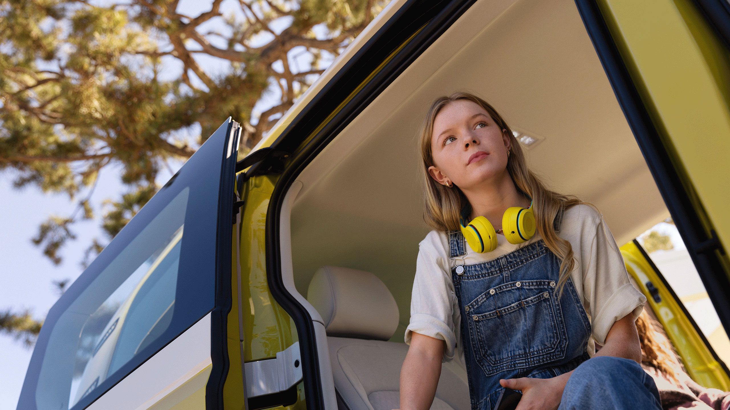 Ein Mädchen mit gelben Kopfhörern sitzt in der Seitentür des VW ID. Buzz.