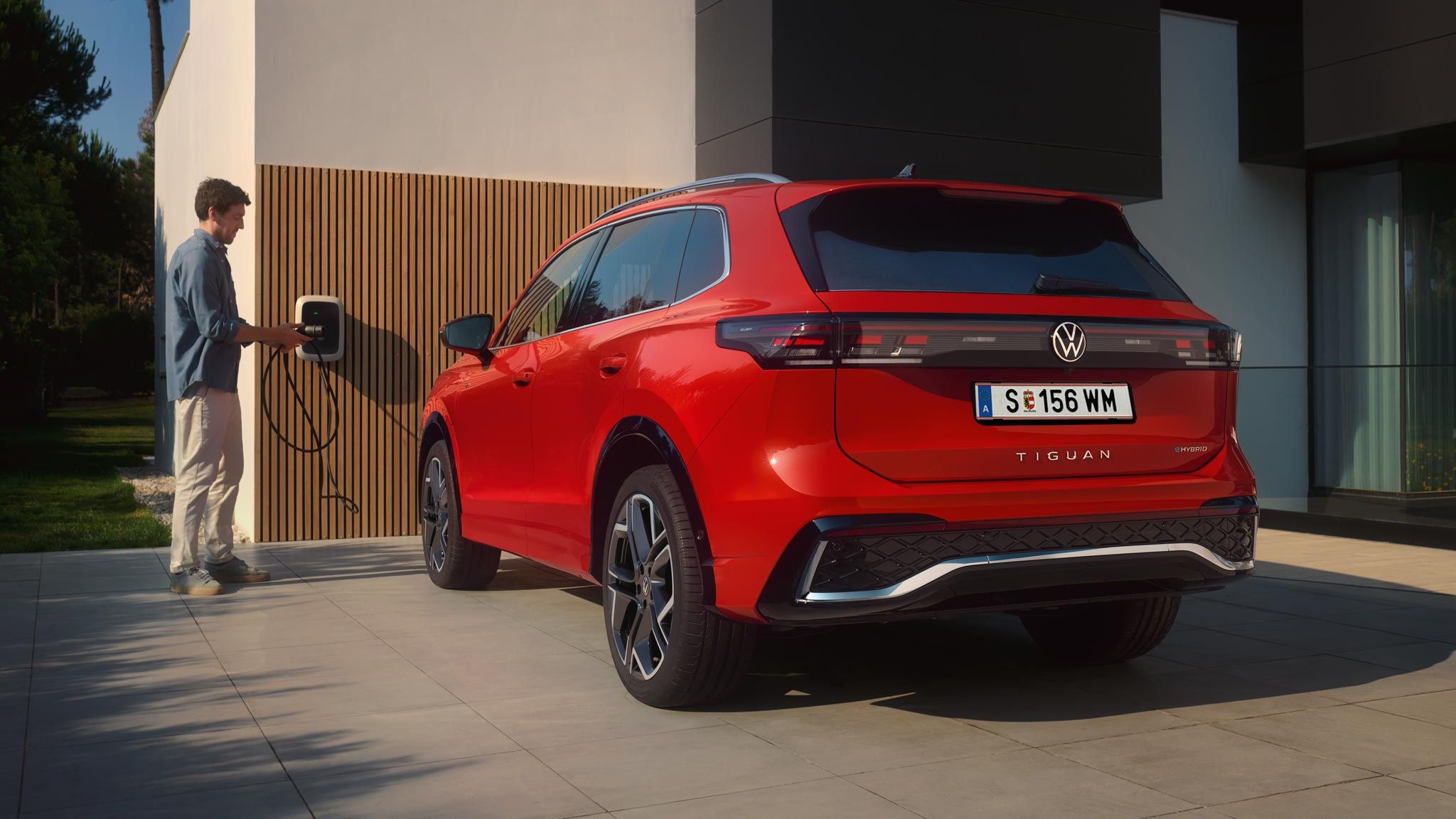 Mann lädt einen roten VW Tiguan eHybrid in der Ausstattungslinie R-Line vor seinem Haus an einer Wallbox