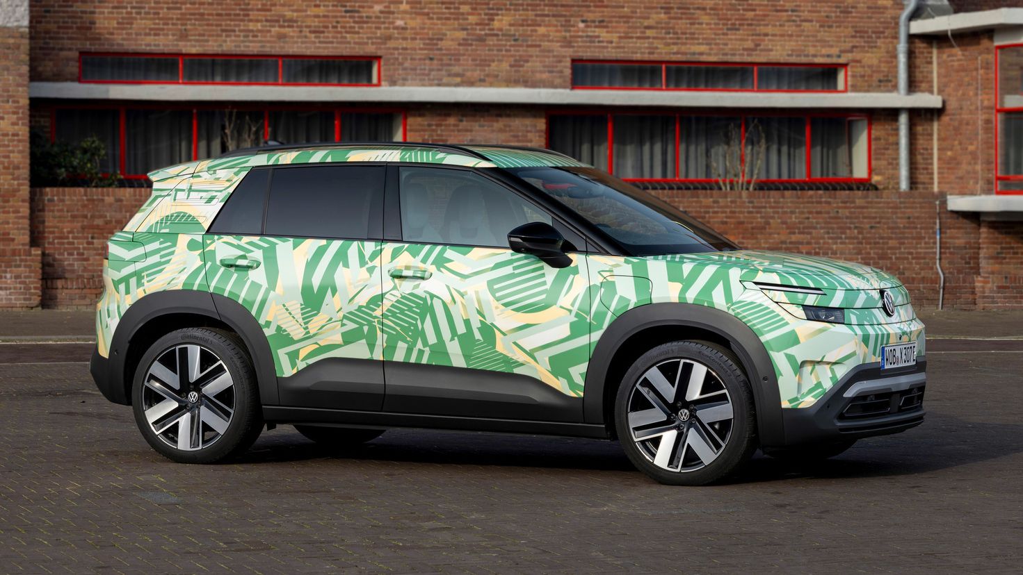 Ein SUV steht vor einem Backsteingebäude. Das Auto hat eine auffällige grüne und weiße Tarnlackierung. Die Fenster des Gebäudes sind rot umrahmt.