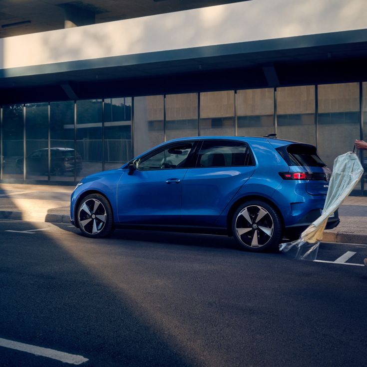 Ein blauer VW ID. Polo Style steht seitlich parkend am Straßenrand, eine Frau geht auf das Fahrzeug zu.