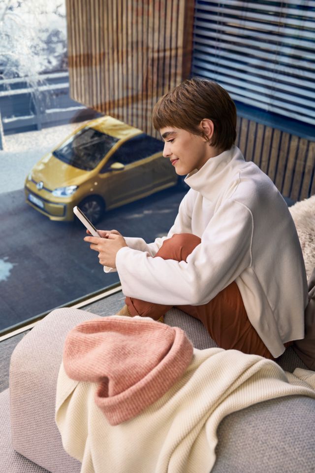 Frau sitzt auf dem Balkon und verbindet sich über das Handy mit ihrem e-up! 