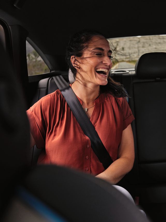 2 Peronen sitzen auf der Rückbank eines Volkswagen und schauen lächelnd auf ein Mobiltelefon