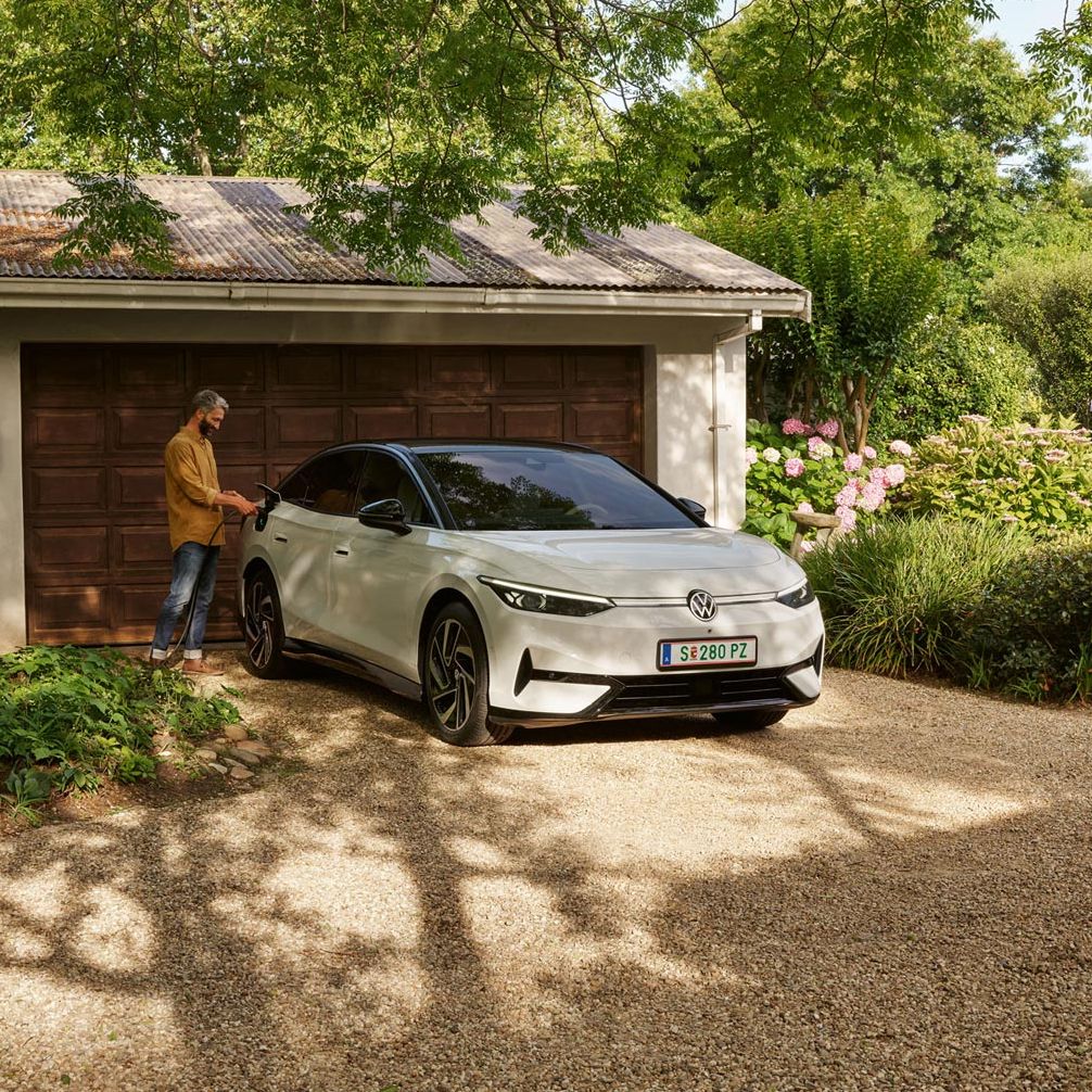 Mann lädt seien weißen VW ID.7 vor seiner Garage mit einer Wallbax