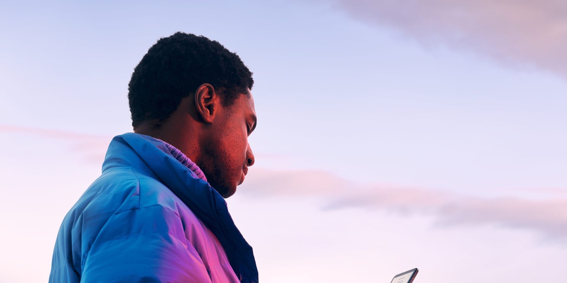 Ein Mann in Winterjacke steht in verschneiter Landschaft und schaut auf sein Smartphone.