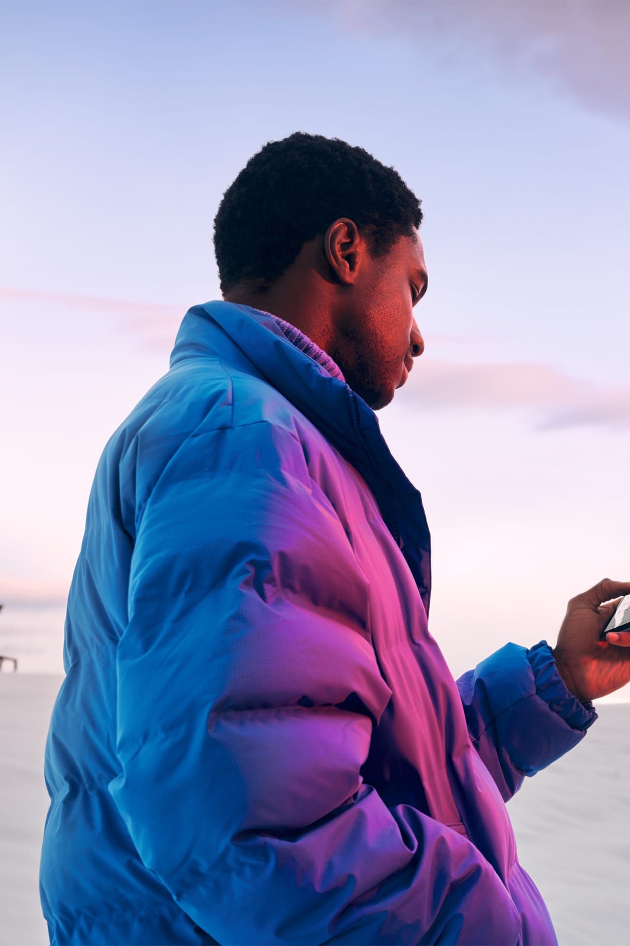 Ein Mann in Winterjacke steht in verschneiter Landschaft und schaut auf sein Smartphone.