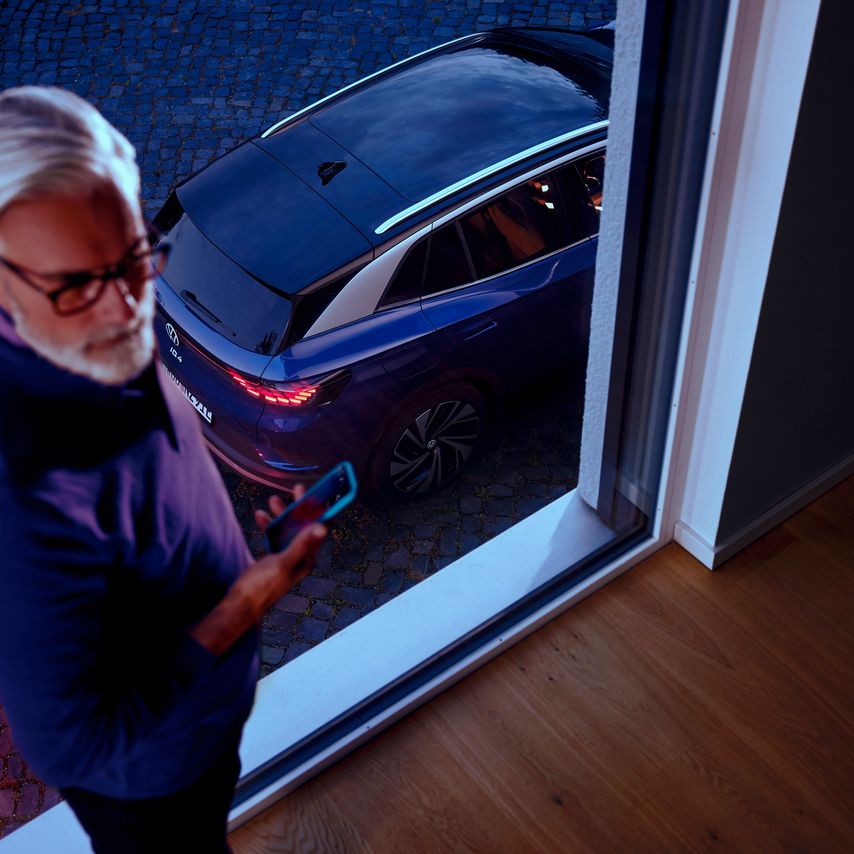 Seitenansicht eines roten VW ID.4 GTX vor Bergkulisse, im Vordergrund blickt eine Frau zum Auto