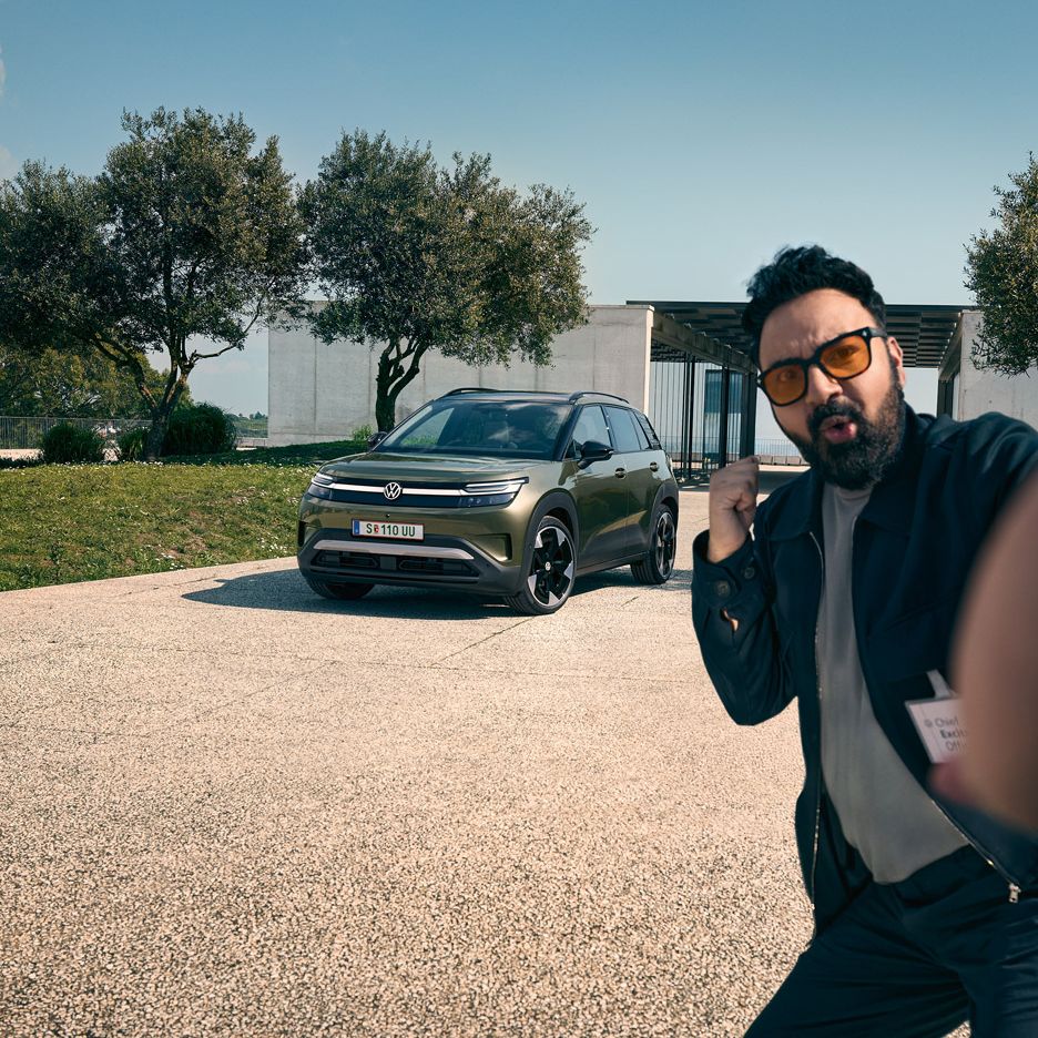 Ein Mann macht ein Selfie mit einem grünen VW ID. Cross, der auf der Auffahrt eines Gebäudes parkt.