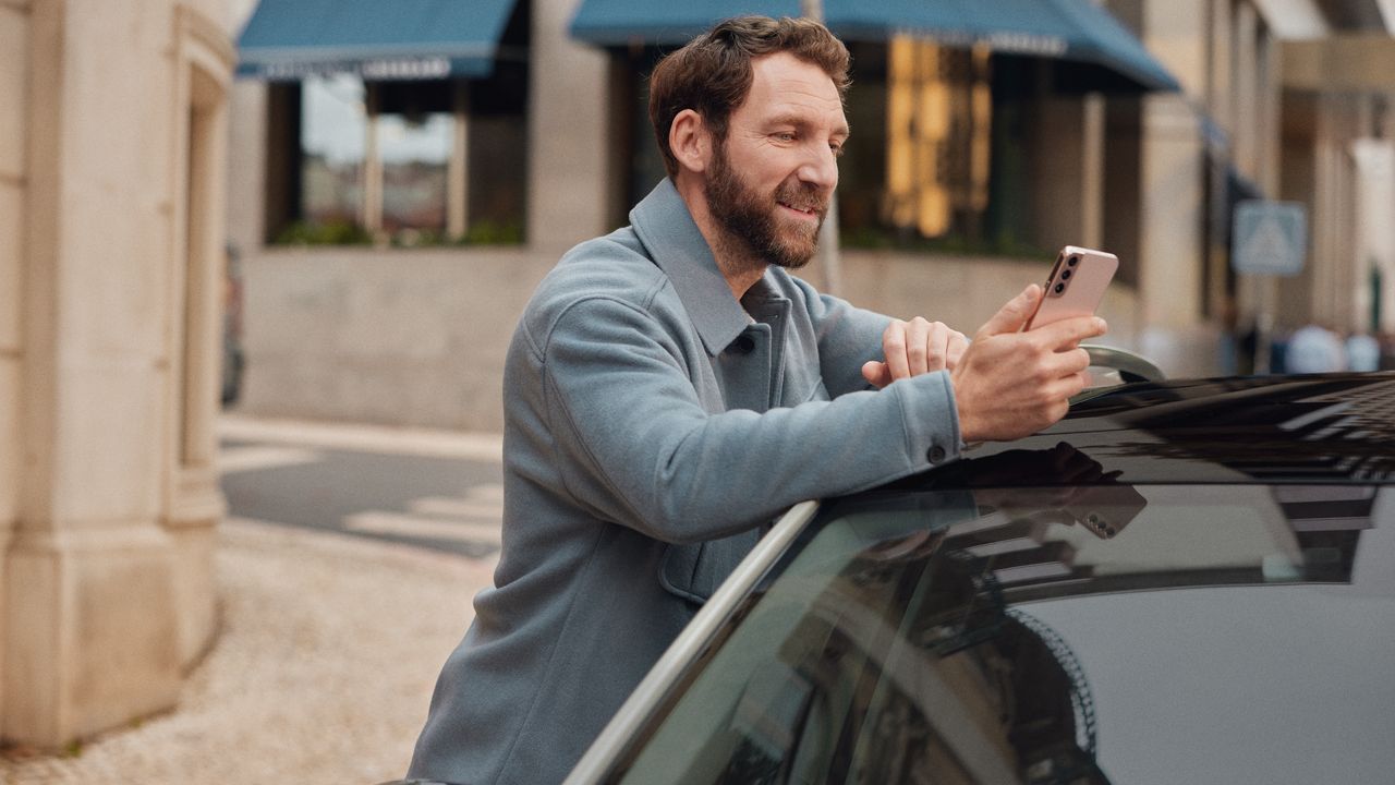 Person lehnt an einem Volkswagen ID. und hält ein Smartphone in der Hand