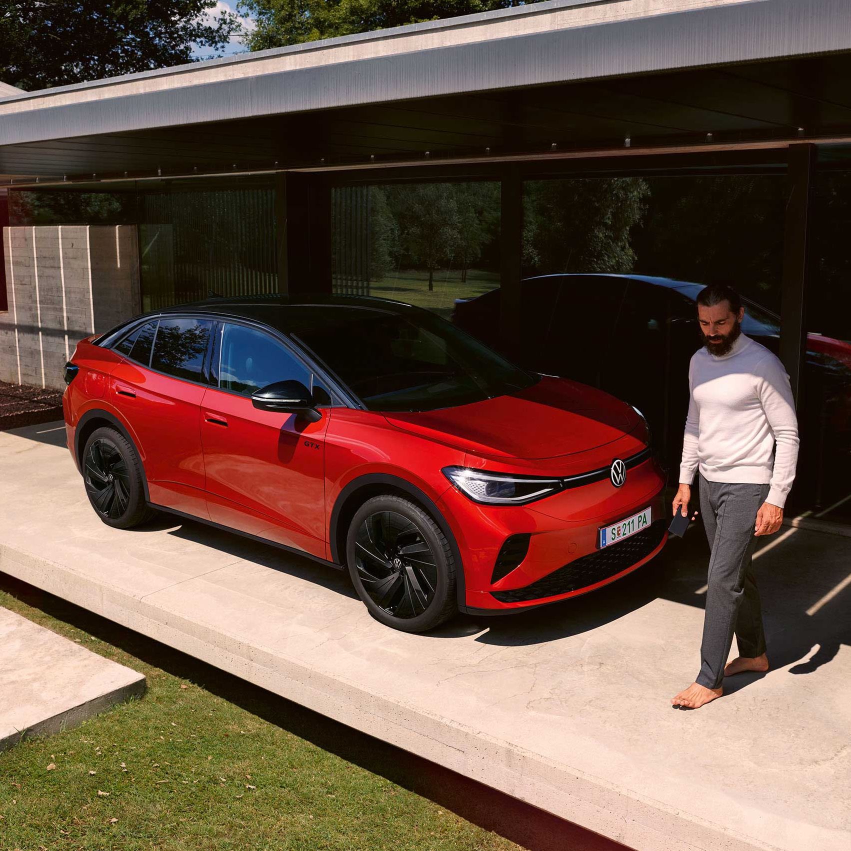 Roter VW ID.5 GTX von schräg vorne in einem modernen Carport, ein Mann geht vor der Motorhaube entlang