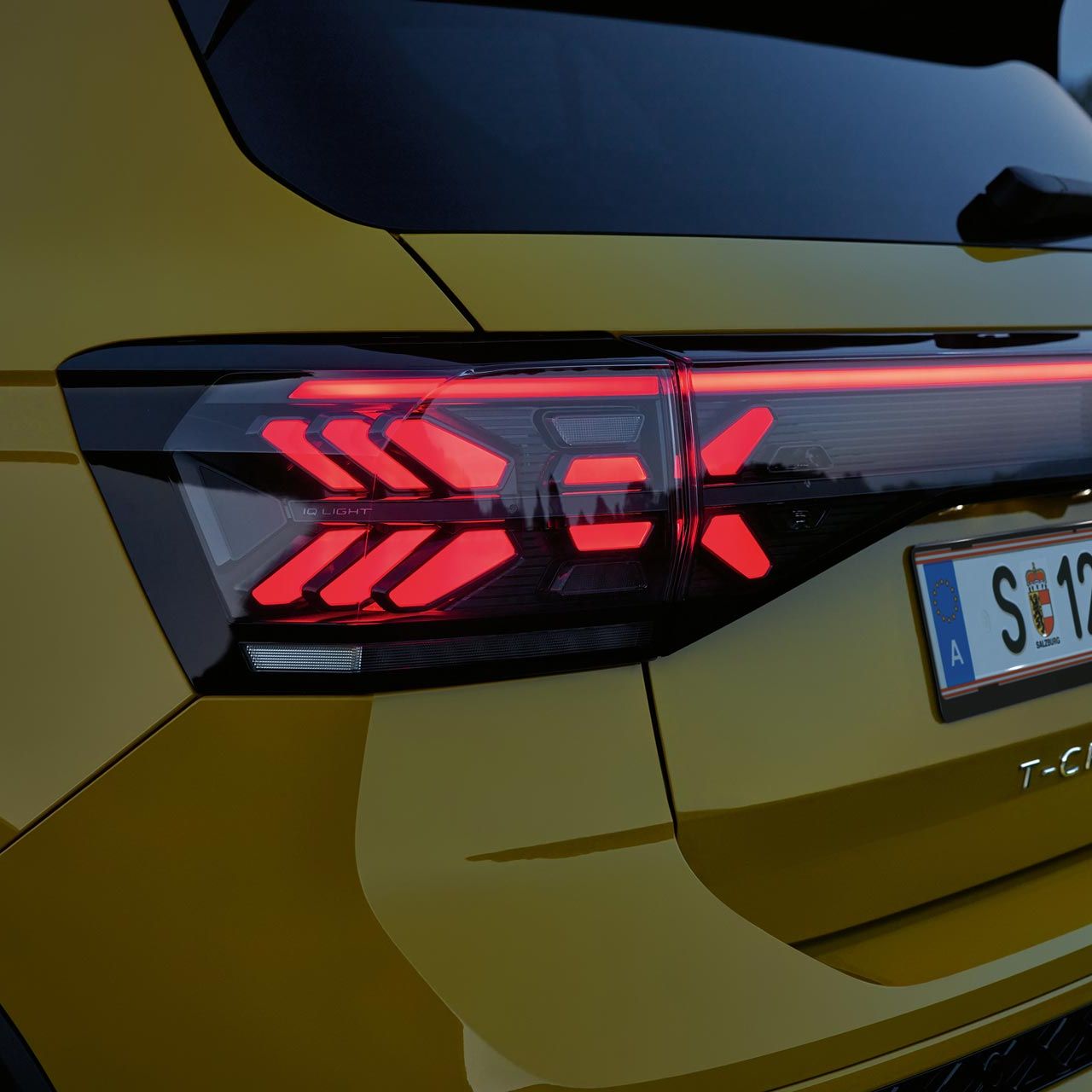 IQ. LIGHT Rückbeleuchtung eines gelben VW T-Cross in Großaufnahme in der Dämmerung.