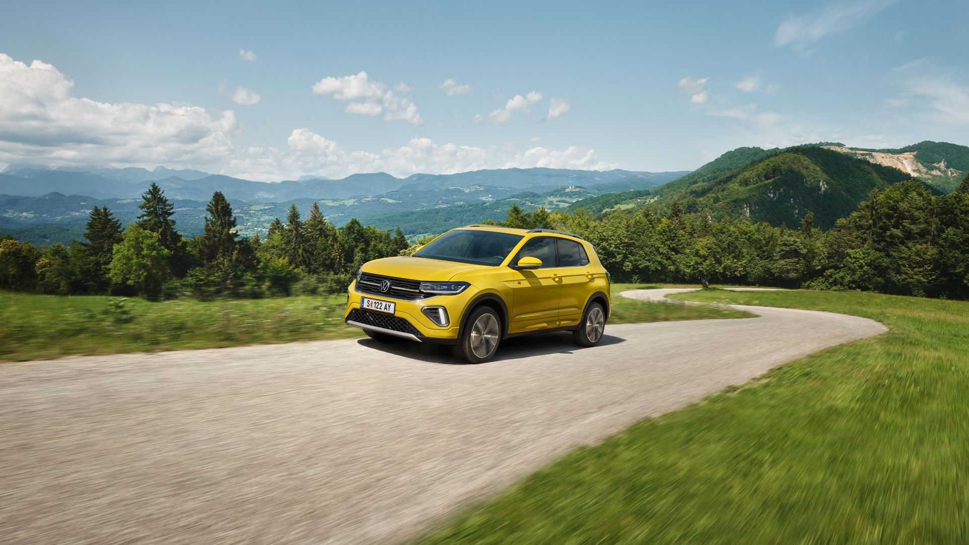 Ein gelber VW T-Cross auf einer Straße in hügeliger Landschaft.
