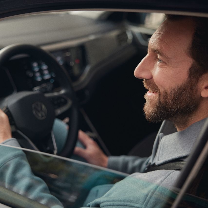 Ein Mann sitzt am Steuer eines Volkswagen und lächelt