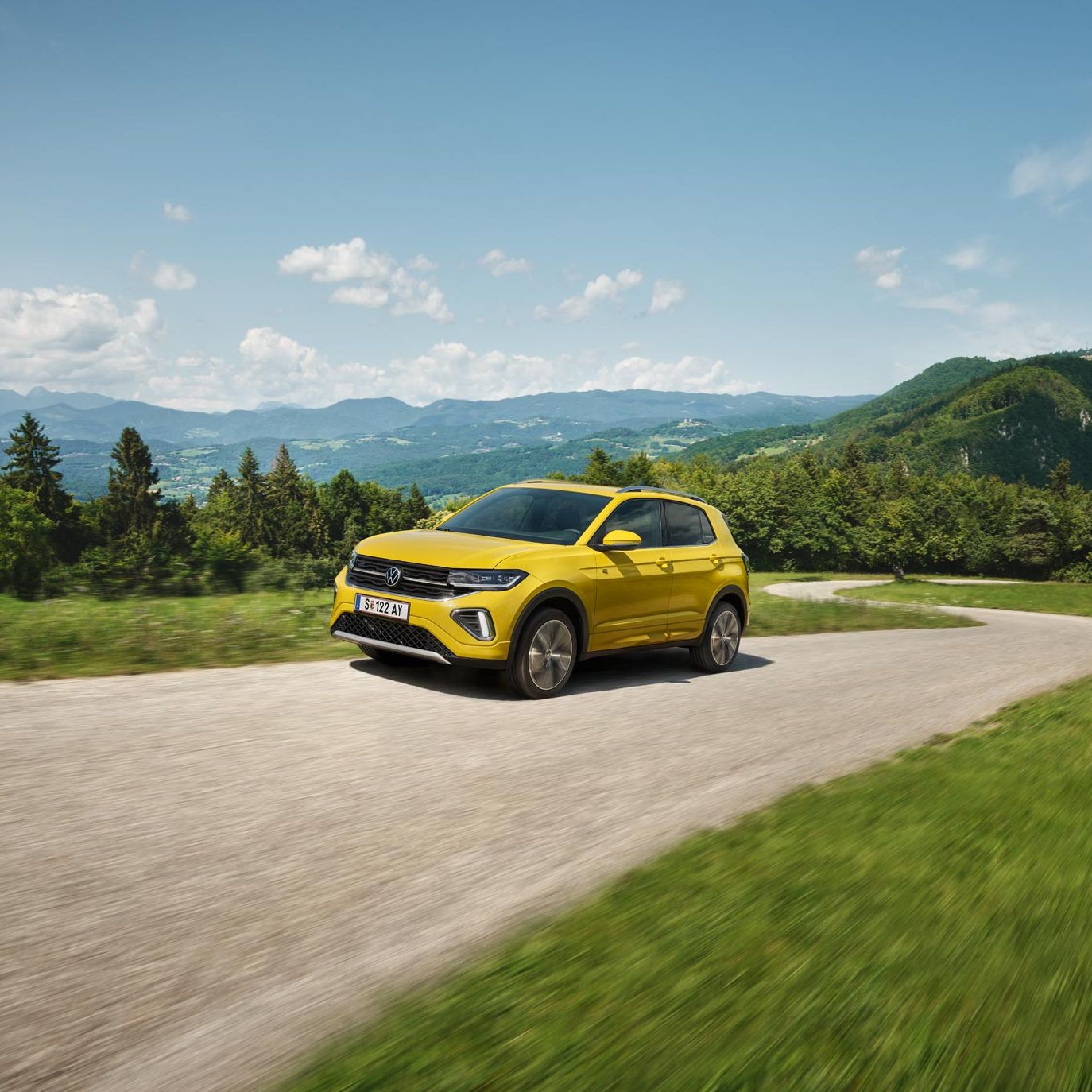 Ein gelber VW T-Cross auf einer Straße in hügeliger Landschaft.