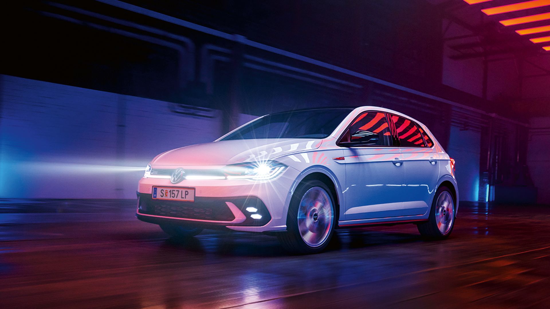 Ein weißer VW Polo GTI fährt in einer Halle mit eingeschalteten LED-Matrix-Scheinwerfern und Lichtleiste in der Front
