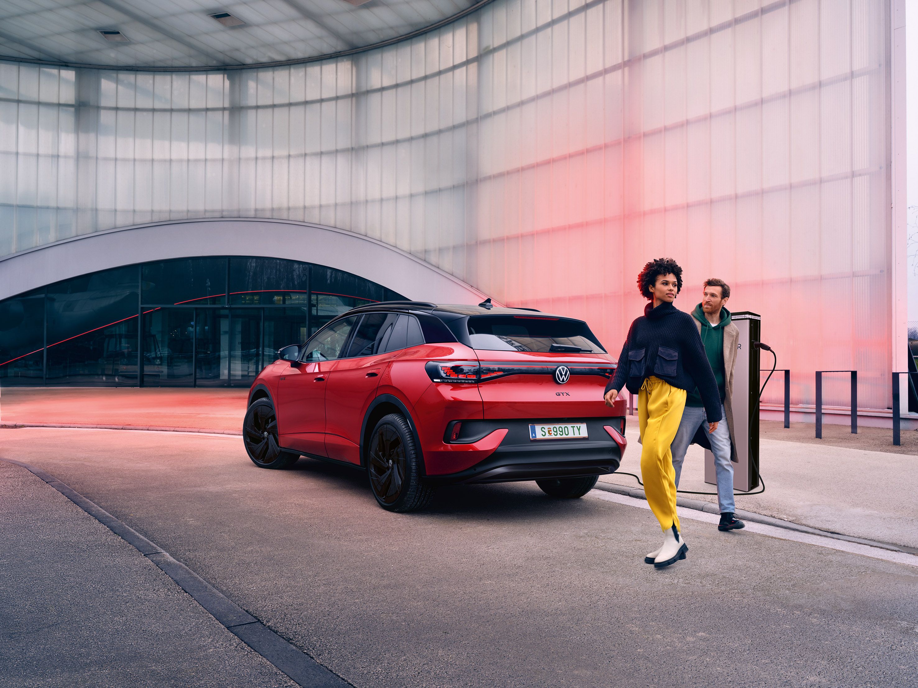 Heckansicht eines roten VW ID.4 GTX, davor überqueren zwei Personen die Straße
