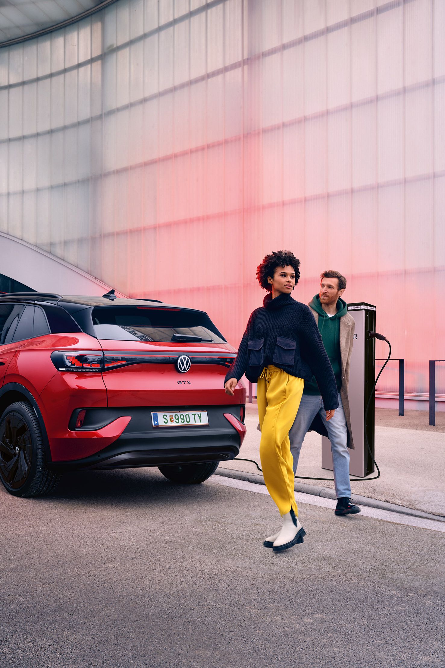 Heckansicht eines roten VW ID.4 GTX, davor überqueren zwei Personen die Straße