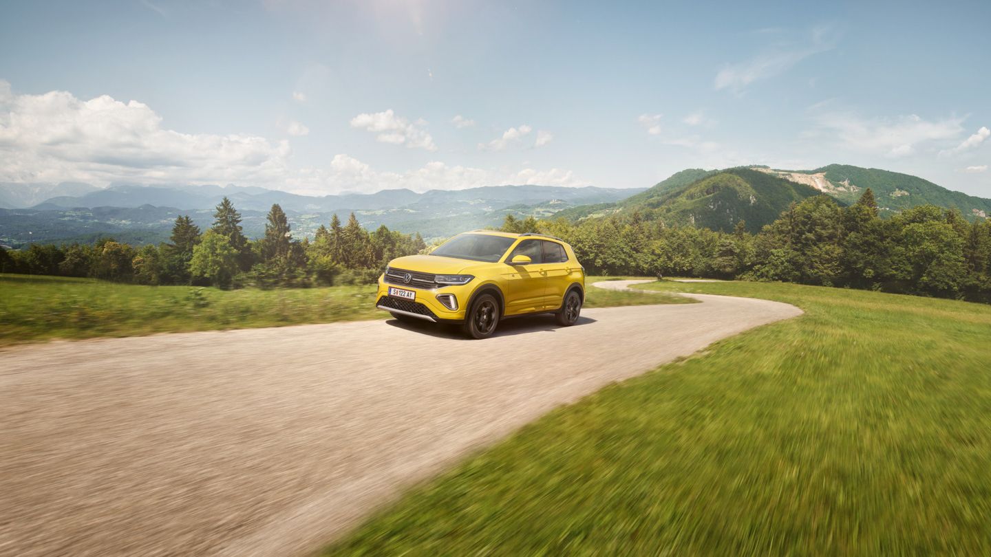 Ein gelber VW T-Cross auf einer Straße in hügeliger Landschaft.