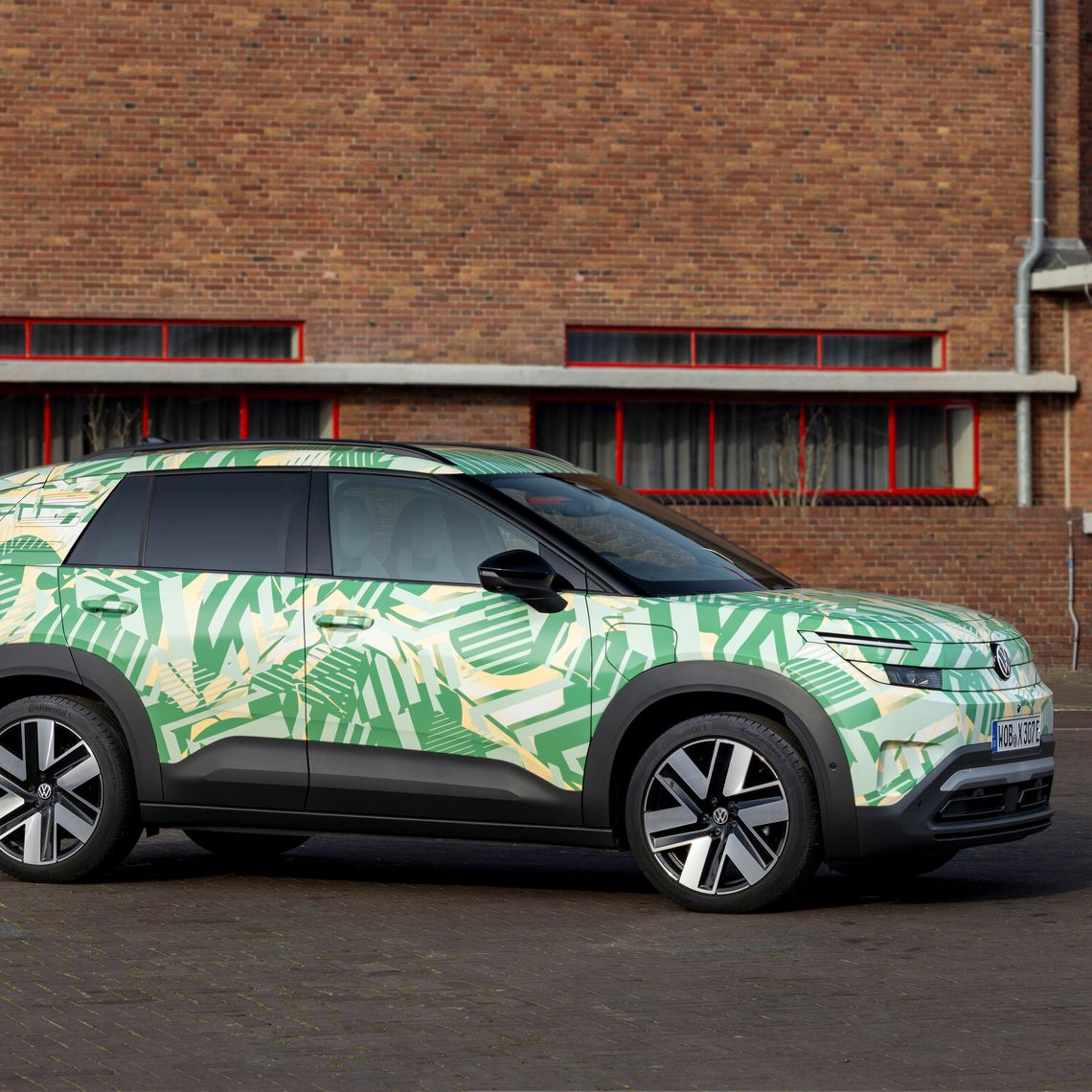 Ein SUV steht vor einem Backsteingebäude. Das Auto hat eine auffällige grüne und weiße Tarnlackierung. Die Fenster des Gebäudes sind rot umrahmt.